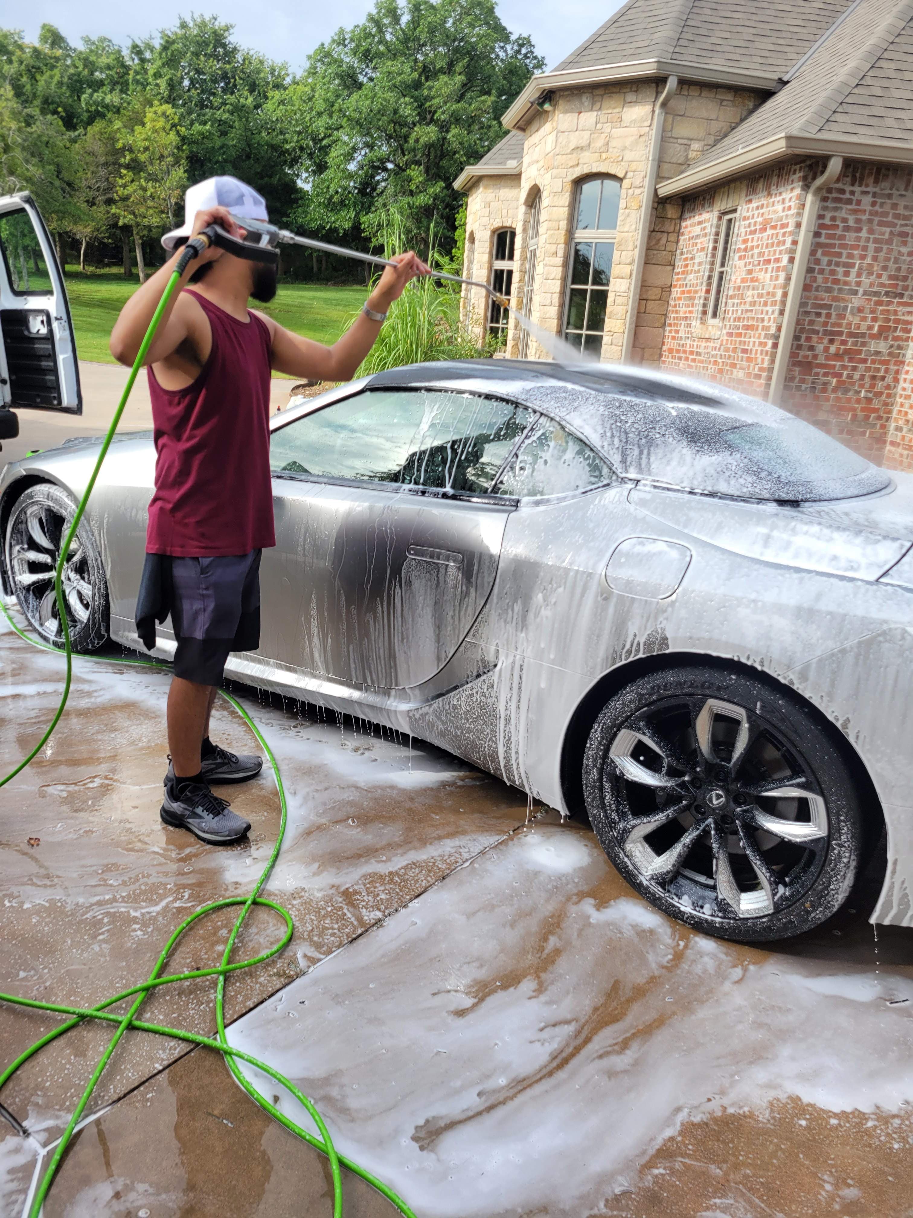 A detailer washing a silver Lexus LC500 with foam.